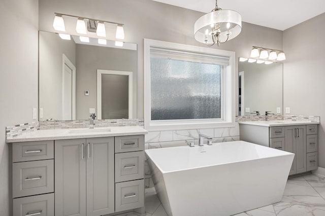 full bathroom with marble finish flooring, a freestanding bath, a chandelier, and two vanities
