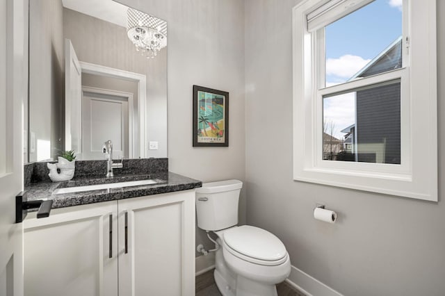 half bathroom featuring baseboards, toilet, vanity, and a chandelier