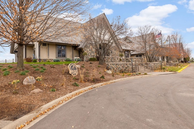 view of front of property with stone siding, fence, and stucco siding