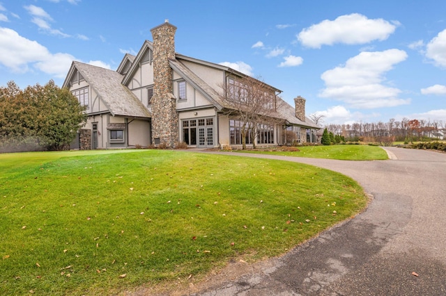 back of house with french doors, a chimney, a yard, stucco siding, and stone siding