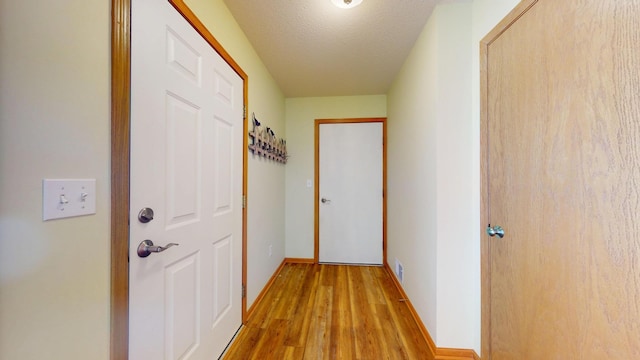 corridor with visible vents, baseboards, light wood-style flooring, and a textured ceiling