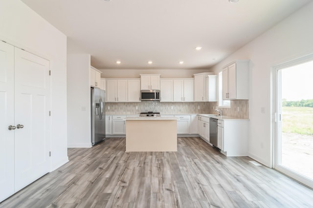 kitchen with sink, a kitchen island, stainless steel appliances, decorative backsplash, and white cabinets