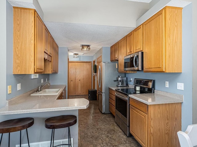 kitchen with a breakfast bar, sink, kitchen peninsula, stainless steel appliances, and a textured ceiling