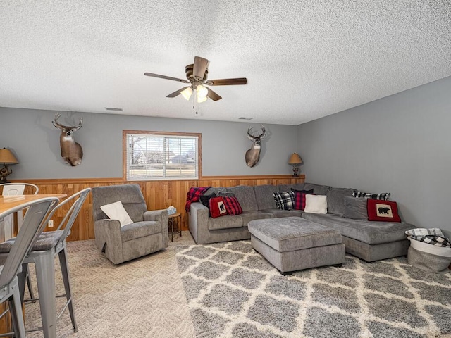 living room with ceiling fan, light colored carpet, wooden walls, and a textured ceiling