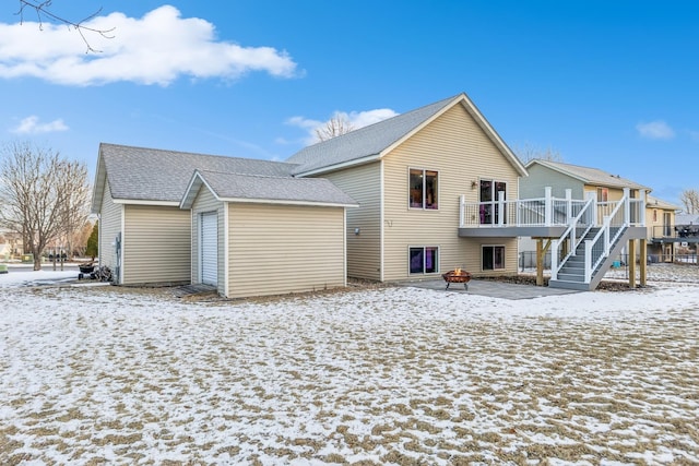 snow covered back of property with an outdoor fire pit and a deck