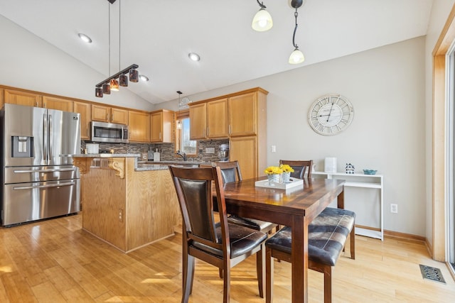 dining room featuring lofted ceiling, sink, and light hardwood / wood-style floors