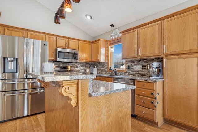 kitchen with appliances with stainless steel finishes, backsplash, light stone countertops, a kitchen island, and vaulted ceiling