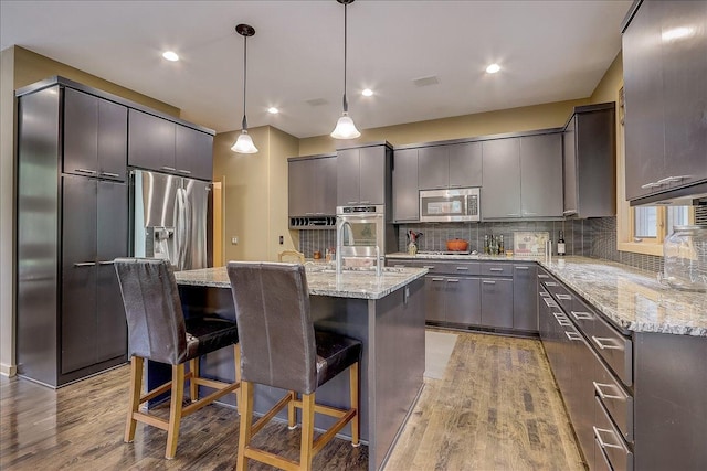 kitchen with a breakfast bar area, hardwood / wood-style floors, stainless steel appliances, an island with sink, and decorative light fixtures