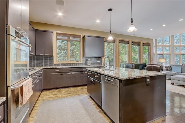 kitchen featuring appliances with stainless steel finishes, decorative light fixtures, tasteful backsplash, an island with sink, and sink