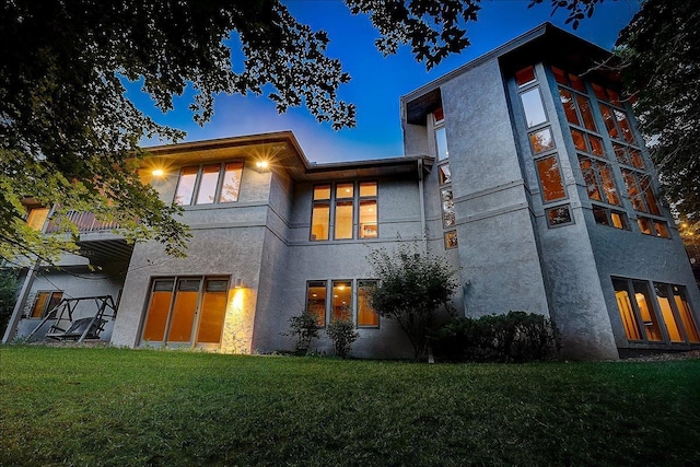 back house at dusk featuring a lawn