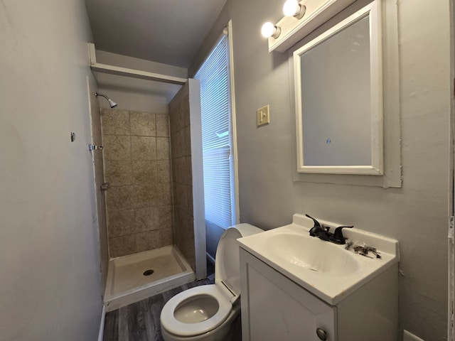 bathroom featuring hardwood / wood-style flooring, tiled shower, vanity, and toilet