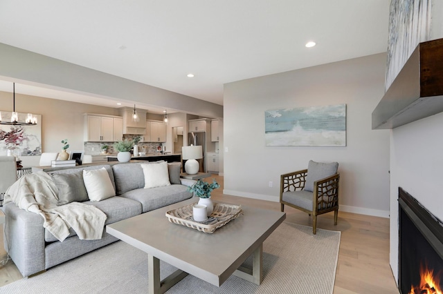 living room with light wood-style flooring, recessed lighting, baseboards, a chandelier, and a warm lit fireplace