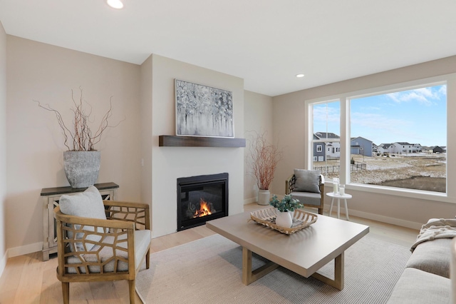 living area with light wood-type flooring, a glass covered fireplace, recessed lighting, and baseboards
