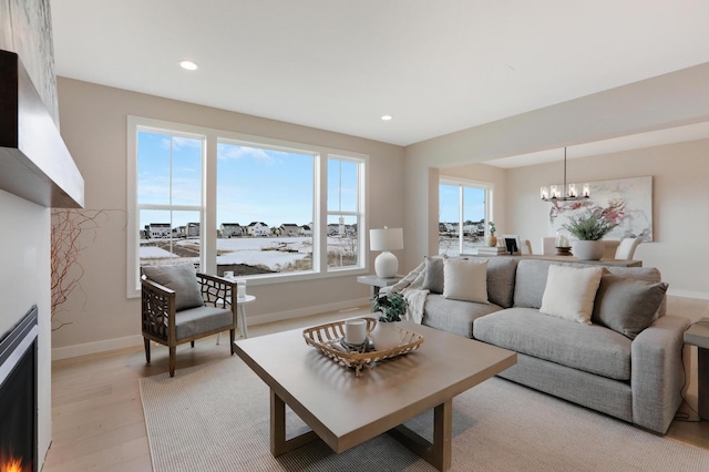 living area with a chandelier, light wood finished floors, recessed lighting, baseboards, and a lit fireplace