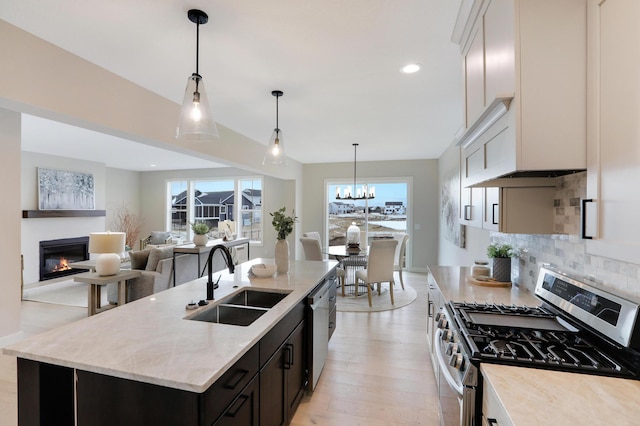 kitchen with appliances with stainless steel finishes, a glass covered fireplace, a sink, tasteful backsplash, and light stone counters