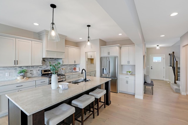 kitchen featuring appliances with stainless steel finishes, a sink, backsplash, an island with sink, and a kitchen bar