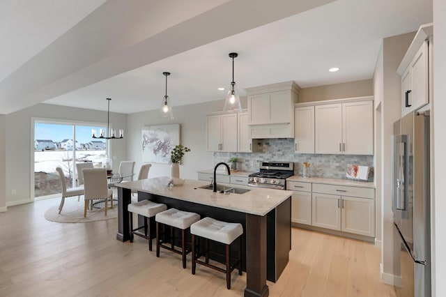 kitchen featuring stainless steel appliances, a sink, tasteful backsplash, light wood finished floors, and a kitchen breakfast bar