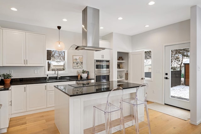 kitchen featuring a kitchen island, island range hood, white cabinetry, sink, and hanging light fixtures