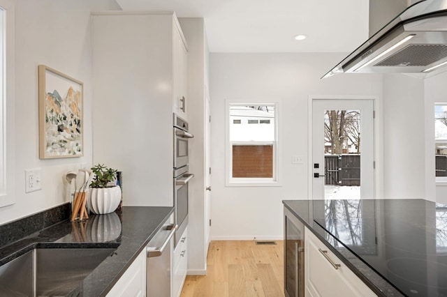 kitchen with white cabinetry, ventilation hood, dark stone counters, beverage cooler, and light hardwood / wood-style floors