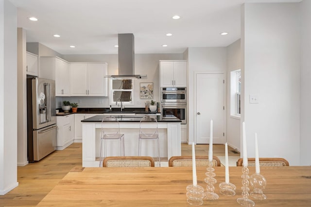 kitchen featuring a breakfast bar, white cabinetry, island range hood, appliances with stainless steel finishes, and a kitchen island