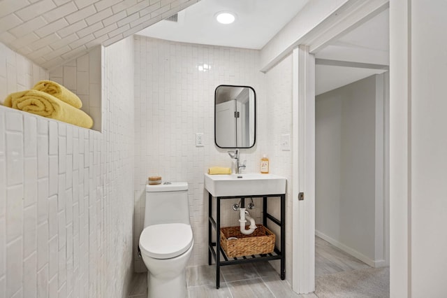 bathroom with toilet, vaulted ceiling, and tile walls