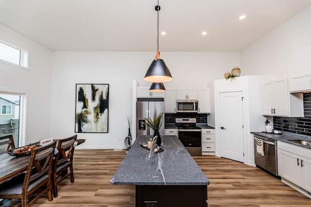 kitchen featuring white cabinetry, a center island, hanging light fixtures, dark stone counters, and stainless steel appliances