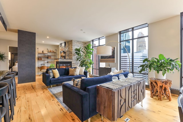 living room featuring a stone fireplace, light hardwood / wood-style floors, and a wall of windows