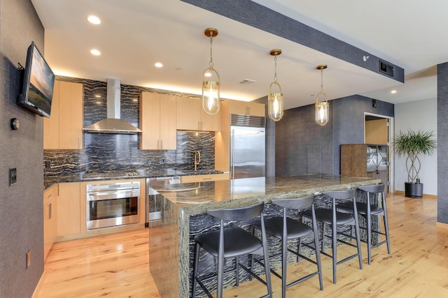 kitchen with appliances with stainless steel finishes, sink, wall chimney range hood, and light brown cabinetry