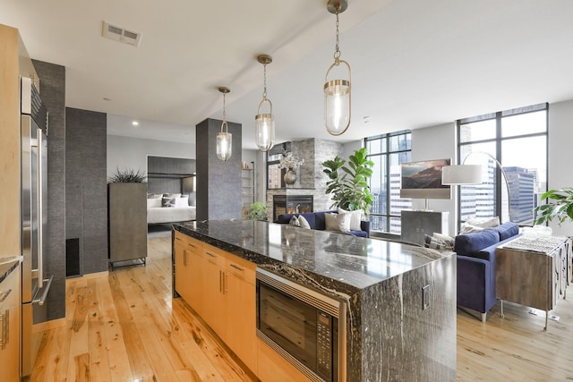 kitchen featuring a kitchen island, pendant lighting, a fireplace, black microwave, and dark stone counters