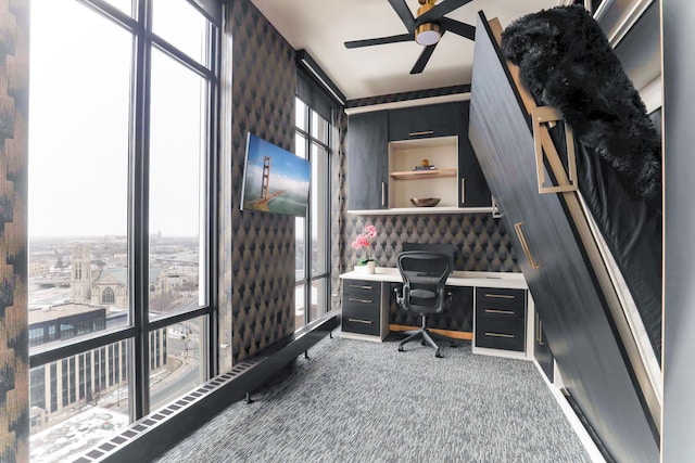 carpeted office space featuring expansive windows and ceiling fan