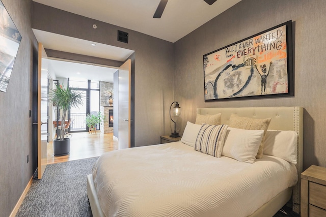 bedroom with expansive windows, ceiling fan, and a stone fireplace