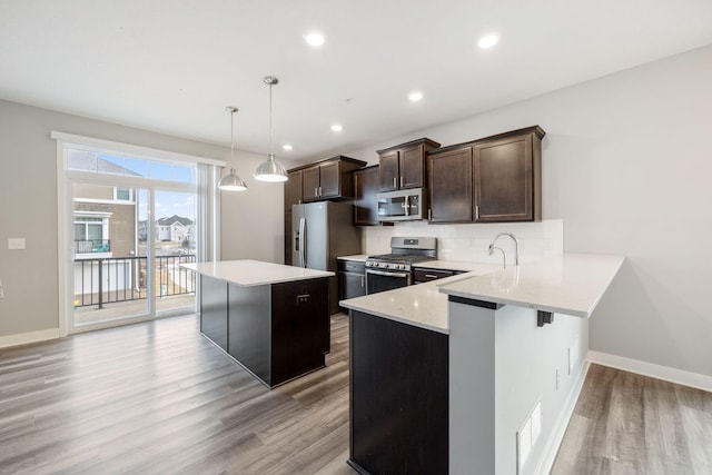 kitchen with a kitchen island, appliances with stainless steel finishes, pendant lighting, a kitchen bar, and kitchen peninsula