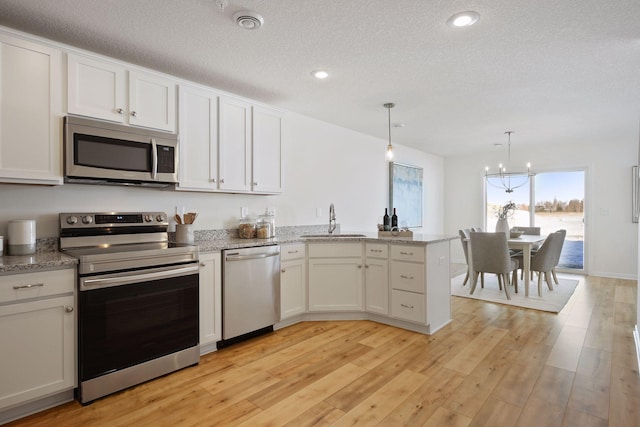 kitchen featuring sink, white cabinetry, hanging light fixtures, stainless steel appliances, and a textured ceiling