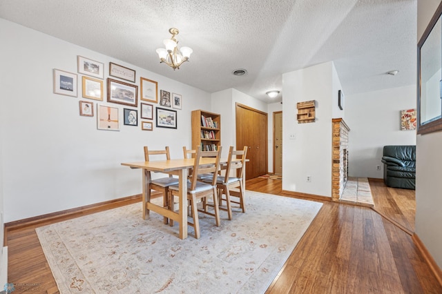 dining room with a textured ceiling, wood-type flooring, and a chandelier