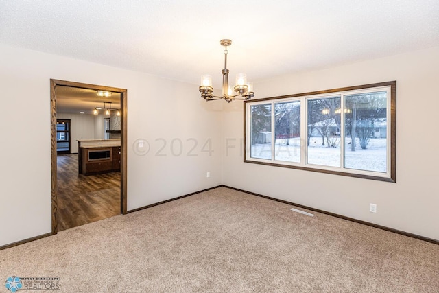 carpeted spare room featuring an inviting chandelier and a textured ceiling