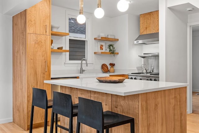 kitchen featuring wall chimney exhaust hood, sink, a breakfast bar area, range, and pendant lighting