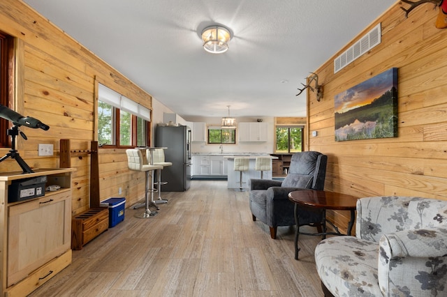 living room featuring a textured ceiling, sink, light hardwood / wood-style flooring, and wood walls