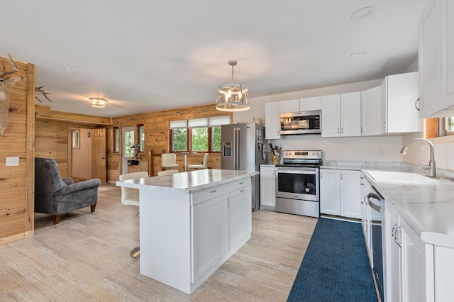 kitchen with pendant lighting, stainless steel appliances, white cabinets, a kitchen island, and wood walls