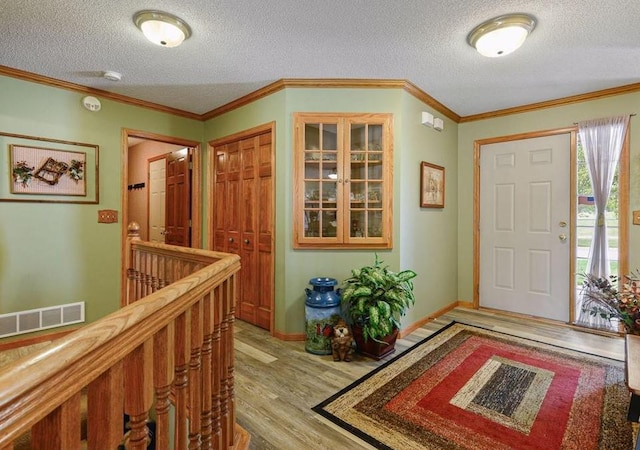 foyer entrance featuring ornamental molding, a textured ceiling, and light wood-type flooring