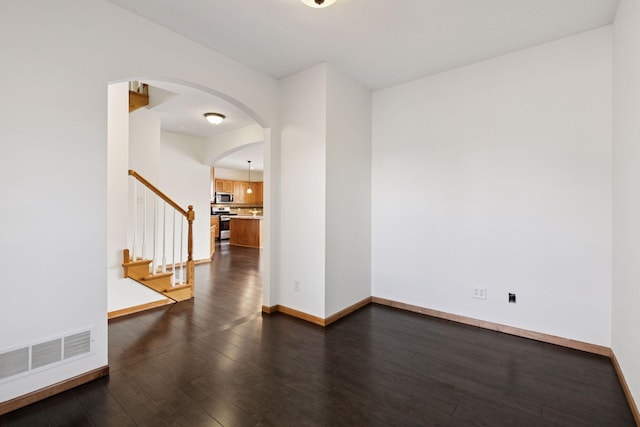 unfurnished room with dark wood-style floors, arched walkways, baseboards, and stairs