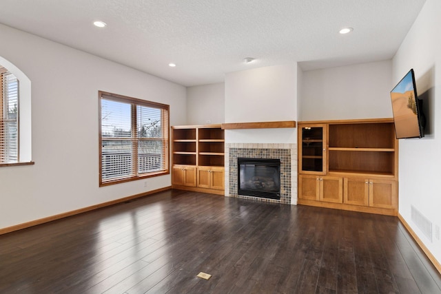 unfurnished living room with dark wood-style floors, a tile fireplace, visible vents, and baseboards