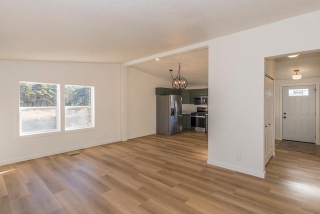 unfurnished living room with lofted ceiling, light hardwood / wood-style floors, and a notable chandelier