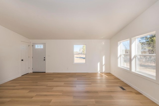 spare room featuring vaulted ceiling, a healthy amount of sunlight, and light hardwood / wood-style flooring