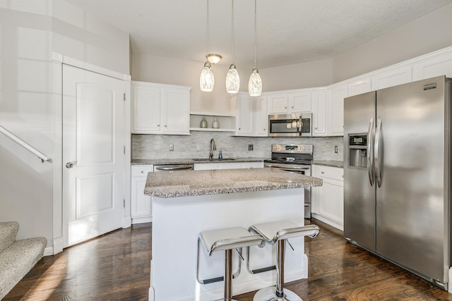 kitchen featuring appliances with stainless steel finishes, white cabinets, decorative backsplash, hanging light fixtures, and a center island