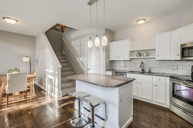 kitchen featuring appliances with stainless steel finishes, decorative light fixtures, white cabinetry, dark stone counters, and a center island