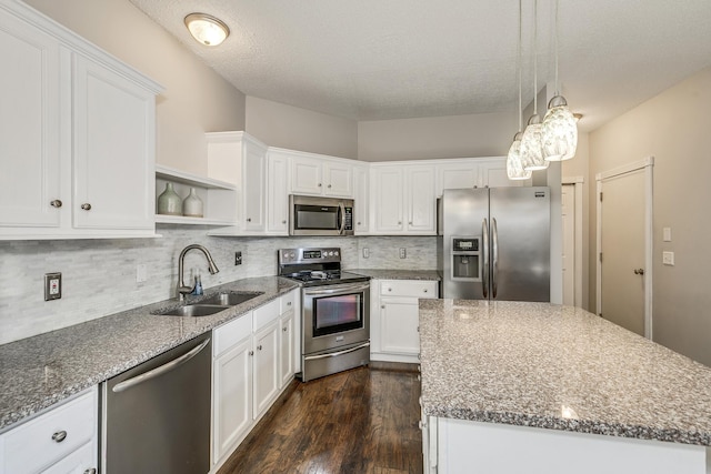 kitchen featuring a kitchen island, appliances with stainless steel finishes, pendant lighting, white cabinetry, and sink