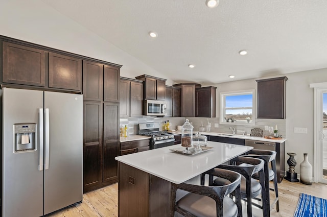 kitchen with vaulted ceiling, appliances with stainless steel finishes, a kitchen breakfast bar, a kitchen island, and backsplash