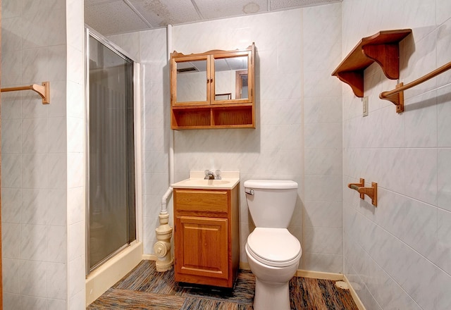 bathroom with a shower with shower door, tile walls, hardwood / wood-style flooring, vanity, and toilet