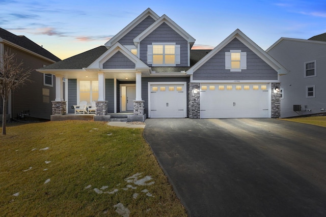 craftsman-style house with aphalt driveway, a porch, a garage, stone siding, and a front yard