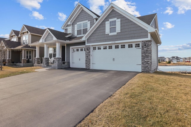 craftsman house with an attached garage, stone siding, a front lawn, and aphalt driveway